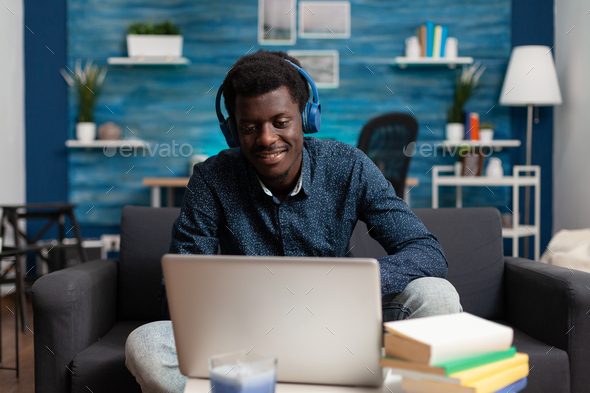 Afro student wearing headphones listening music while typing marketing ideas