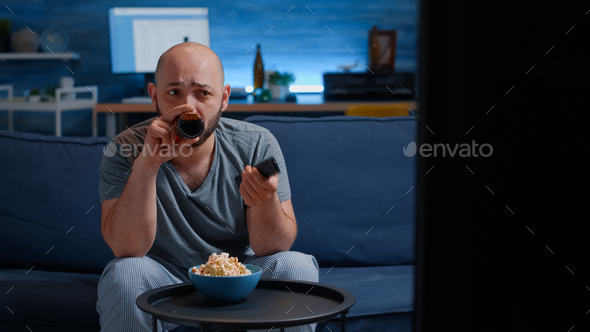 Man relaxing on cozy couch using remote controller switching tv channels