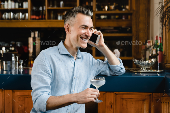 Businessman drinking wine cocktail talking on smartphone with colleagues friends relaxing at bar