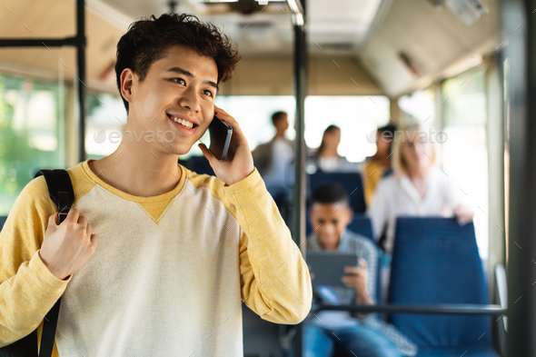 Smiling Asian guy taking bus, talking on cellphone