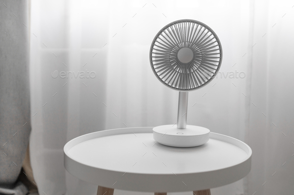 Modern electric portable fan on a white coffee table in bedroom.