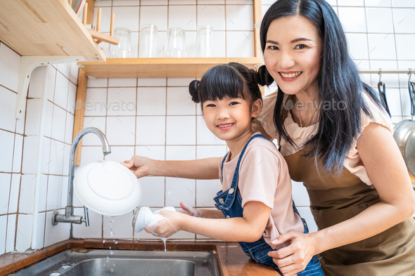 Asian happy family, loving mom teach young girl to wash dishes in house.
