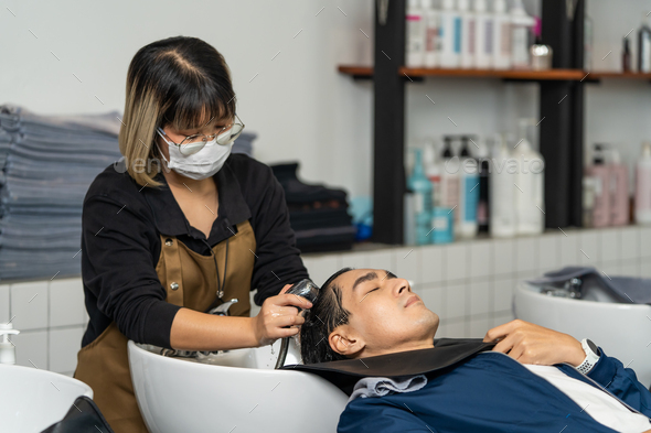 Asian expert Hairdresser massage and washing hair of beautiful young male customer.