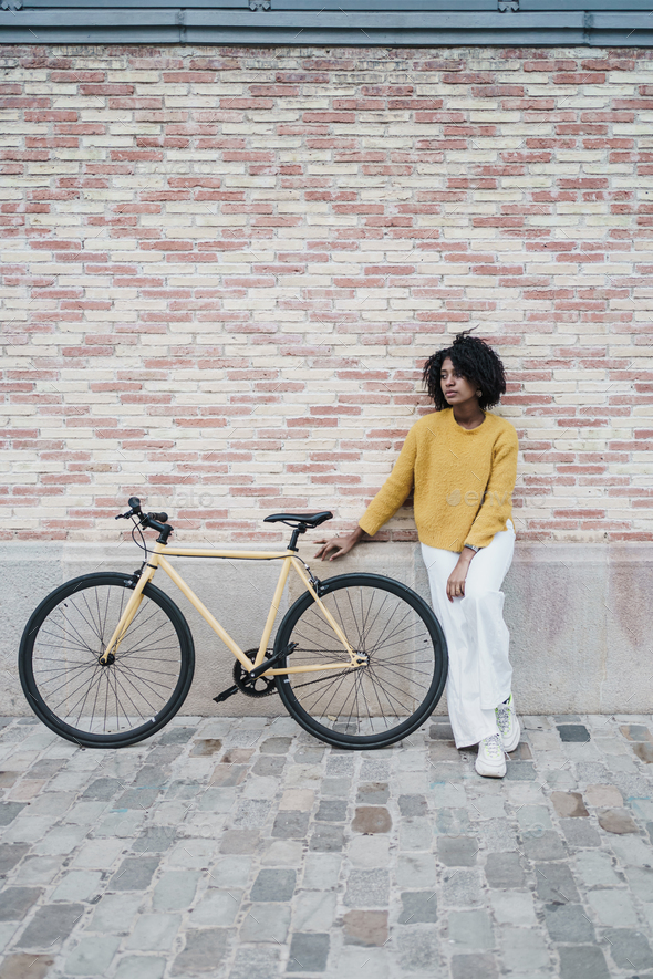 Pensive black woman standing next to a yellow bike. Eco-friendly transportation in the city