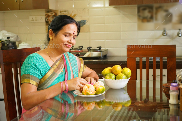Smiling woman with orange at breakfast table - Stock Photo - Images
