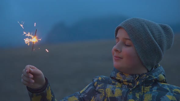 A Boy with a Bengali Fire in His Hand Stands in the Evening Outdoors alt
