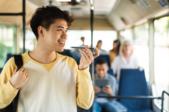 Smiling Asian guy taking bus, talking on cellphone