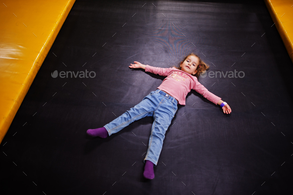 Cute baby girl lying on a trampoline in indoor play center.