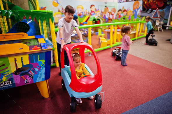 Four kids playing in indoor play center. Kindergarten or preschool play room. Riding toy car.