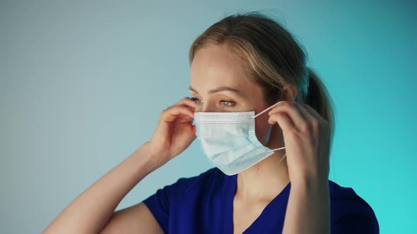 Young Pensive Caucasian Female Surgeon Putting on or Taking Off Her Face Mask alt