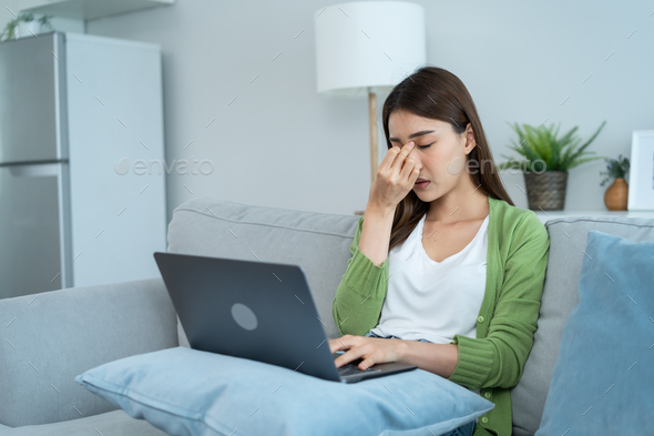 Exhausted Asian business woman hurt eye while using laptop computer.