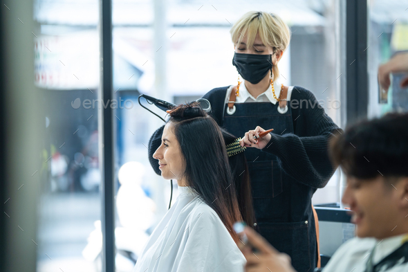 Asian stylist use curling iron make curly to customer\'s hair in salon.