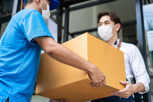 Asian deliver man wear face mask handling box, carrying the package to waiter in coffeehouse.