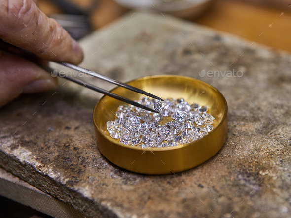 Jewelry production. Diamond held by tweezers against the background of diamonds