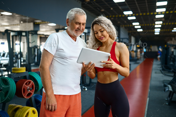 Elderly man and female trainer looks on laptop