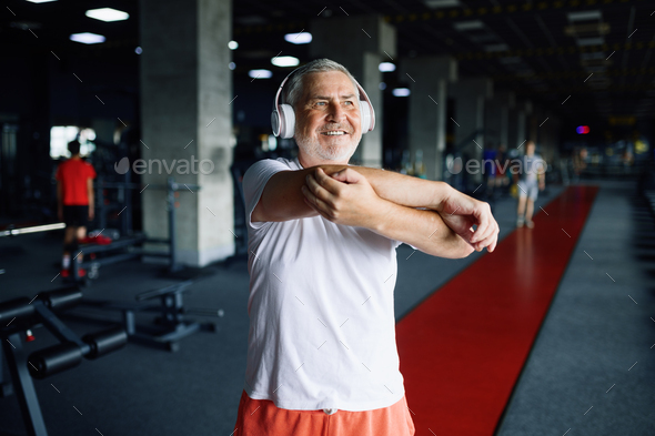 Old man in headphones doing fit exercise, gym
