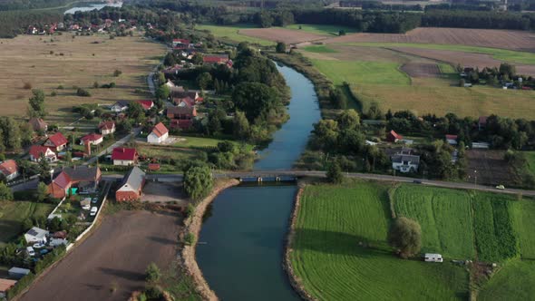 Aerial rural shot of a small village and farms by the river. Camera tilts down to focus on a wooden alt
