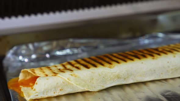 Cheese shawarma with vegetables lies on a foil. Grilled pita with ingredients. Close up. alt