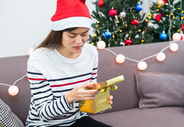 Asian woman upset when open gold xmas gift box at holiday party on sofa