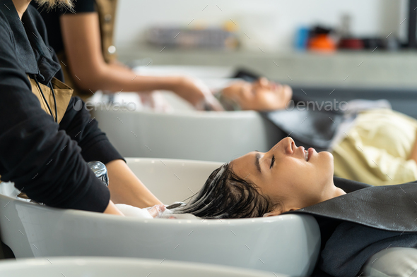 Caucasian young woman lying down on salon washing bed getting hair washed  by professional stylist. Stock Photo by s_kawee