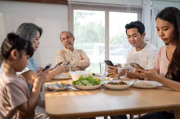 Asian family using mobile phone while eating breakfast not pay attention to Senior old man.