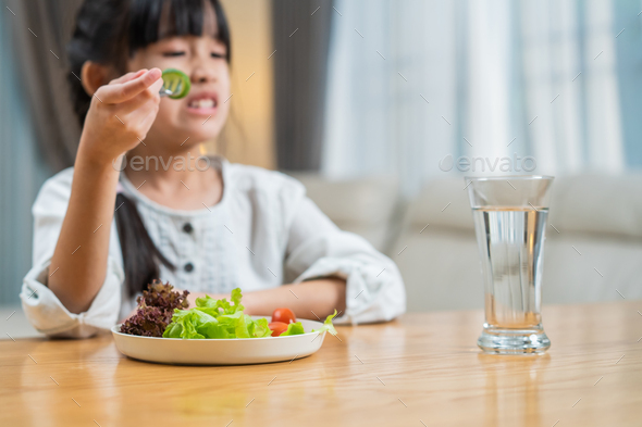 Unhappy Asian little young girl child don\'t want to eat green vegetables on dinner plate.