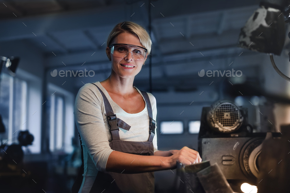Portrait of mid adult industrial woman working indoors in metal workshop, looking at camera