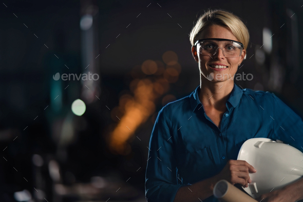 Portrait of mid adult industrial woman working indoors in metal workshop, looking at camera
