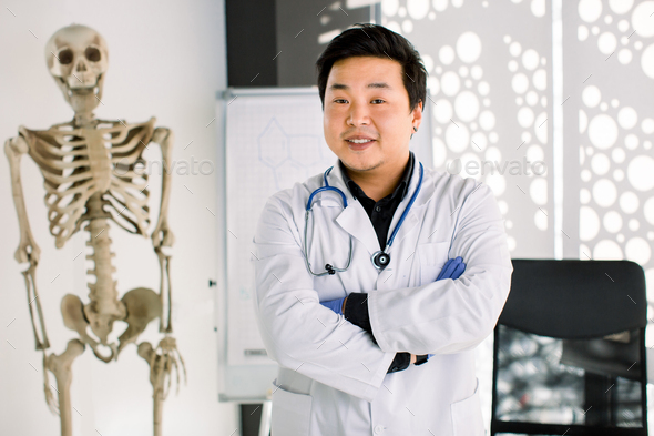 Portrait of friendly Asian Korean doctor man at his office smiling to camera. Young smiling