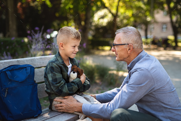 Senior man squatting and talking to grandson outdoors on bench in park - Stock Photo - Images