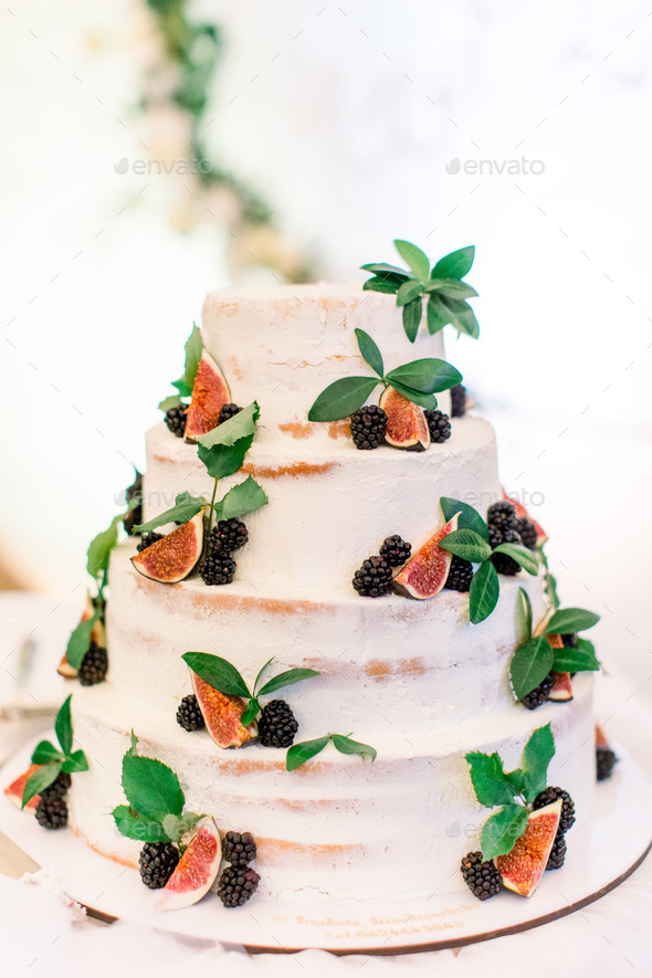 wedding cake with blackberries and figs, green leaves. rustic style. food on a board