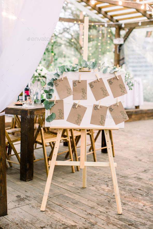 Original rustic wooden board decorated with eucalypthus, guest list, tables on the background in the