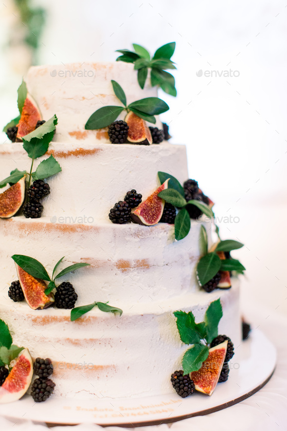 Cake biscuit with figs, blackberries and mint, four-tiered, on a background of white wall