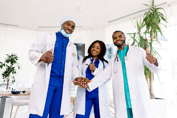 Doctors team. Health care. Three happy African doctors stack hands together as team for motivation
