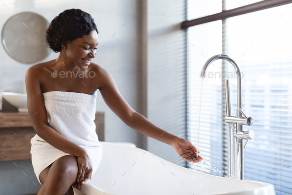 Young black woman preparing to take a bath in bathroom Stock Photo by  Prostock-studio
