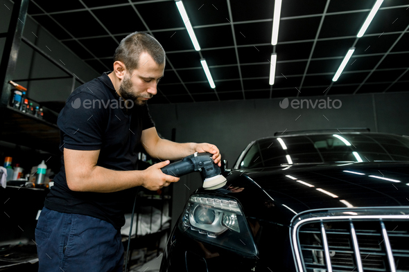 Young handsome Caucasian man, worker of auto detailing service, holds orbital polisher in the hand