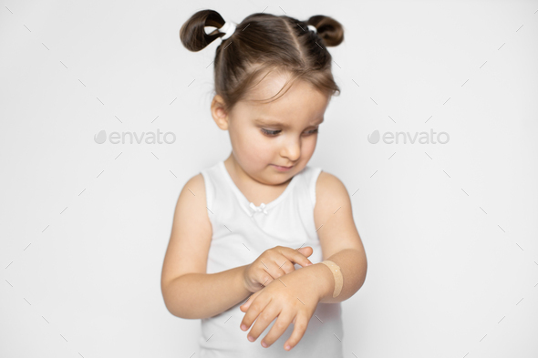 A little cute 3 years old girl with blonde hair demonstrating how to apply adhesive plaster bandage