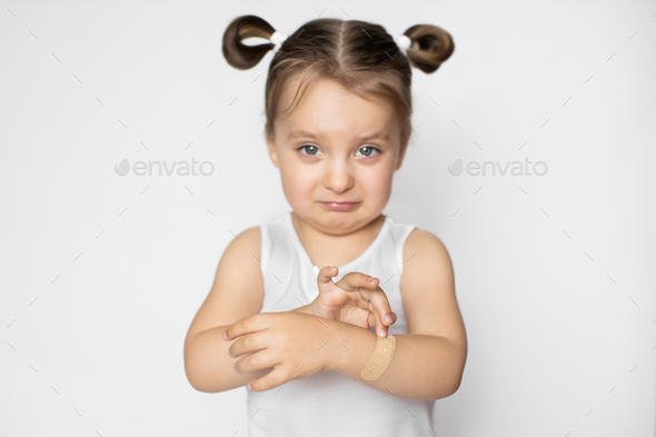 Portrait of cute pretty crying child girl, feeling pain because of wound on her arm, applying