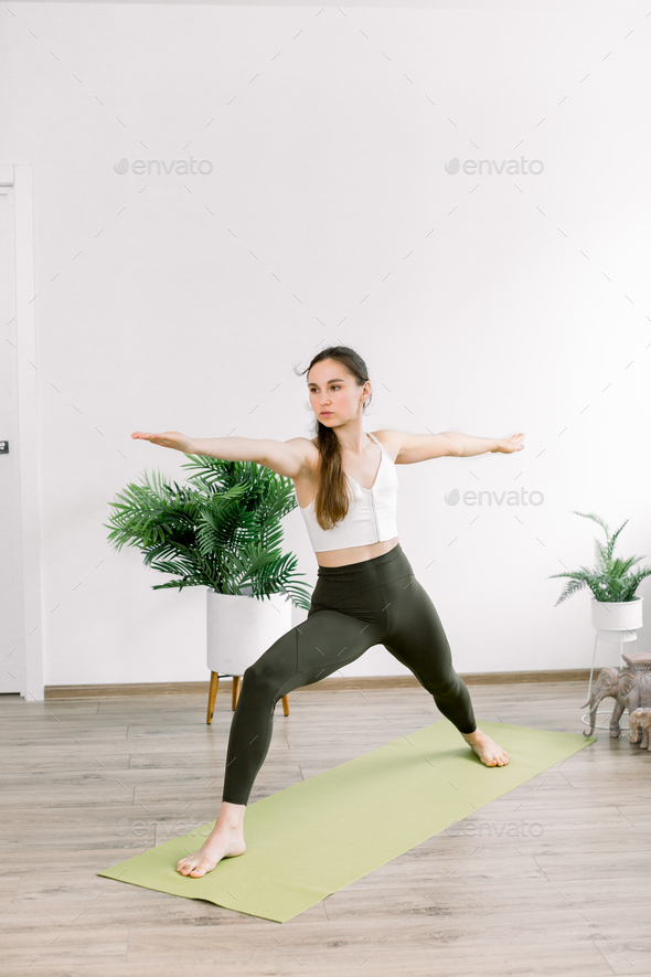 Side angle view of sporty woman practicing yoga, standing in Warrior two exercise, Virabhadrasana II
