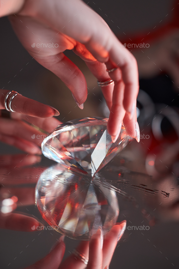 Beauty Woman holds big diamond in hand while lying on table. Beautiful hands, professional manicure