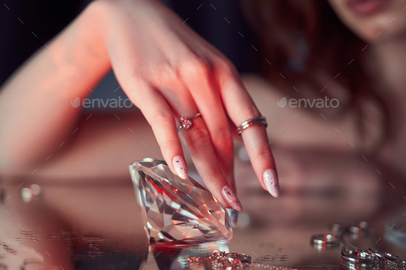 Beauty Woman holds big diamond in hand while lying on table. Beautiful hands, professional manicure