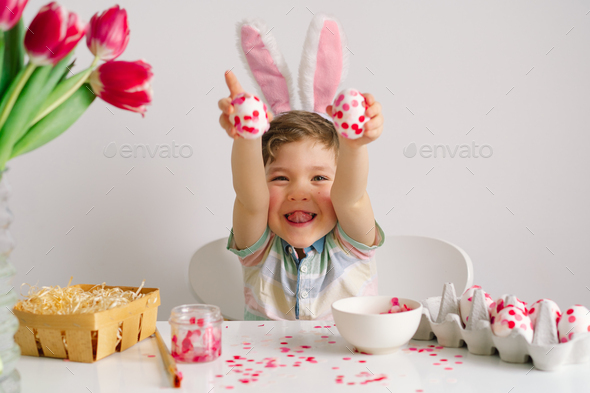 A little boy in bunny ears decorates Easter eggs. Easter concept - Stock Photo - Images