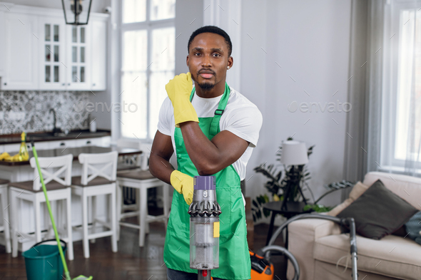 African man in apron and gloves holding vacuum cleaner