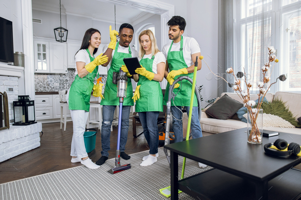Purposeful high skilled multiracial cleaning team checking their responsibilities on tablet pc