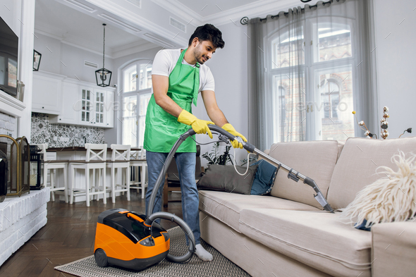 Indian man using vacuum cleaner for cleaning couch