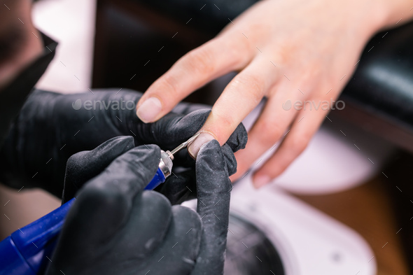 Manicurist use electric nail file drill in beauty salon. Perfect nails manicure process close up