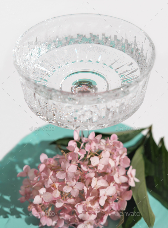 beautiful crystal high glass with mineral water on a turquoise table next to pink hydrangea flowers