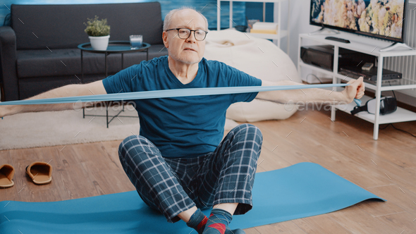 Elder adult sitting on yoga mat and pulling resistance band Stock