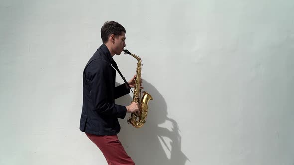 a Man in a Dark Shirt and Red Trousers Plays the Saxophone Emotionally and Casts a Shadow on a White alt
