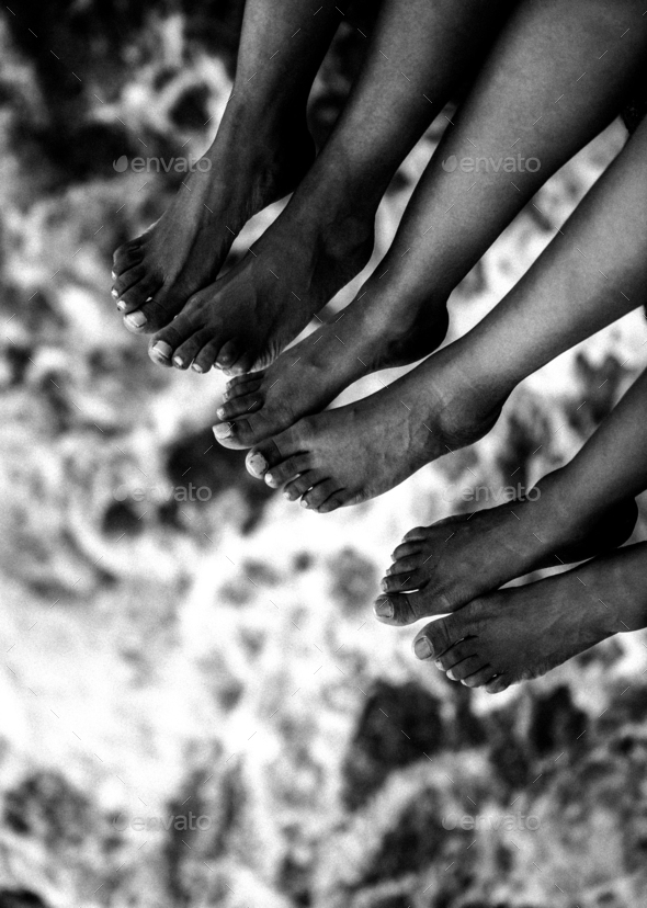 Three sisters feet hanging from a seashore with the ocean below